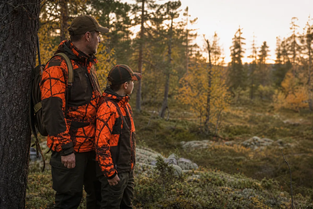 Ung jägare i varm, synlig jaktklädsel tillsammans med vuxen i skogsterräng