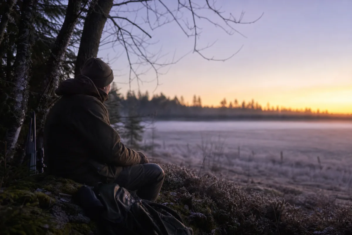 Jägare i varm jaktklädsel sitter stilla på pass i kall gryning