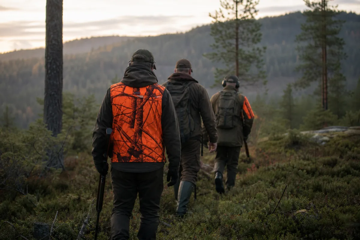 Jägare i tydligt synlig varselfärgad väst bland andra jägare i skogsterräng